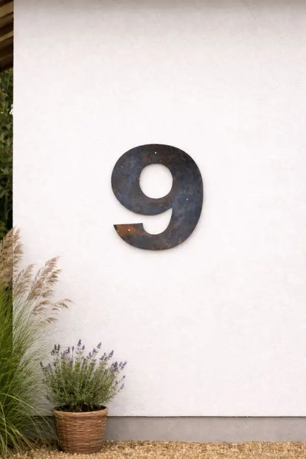 Husnummer i cortenstål monteret på en hvid husmur, hvor tallet er cirka 40 cm højt og fastgjort med synlige skruer.