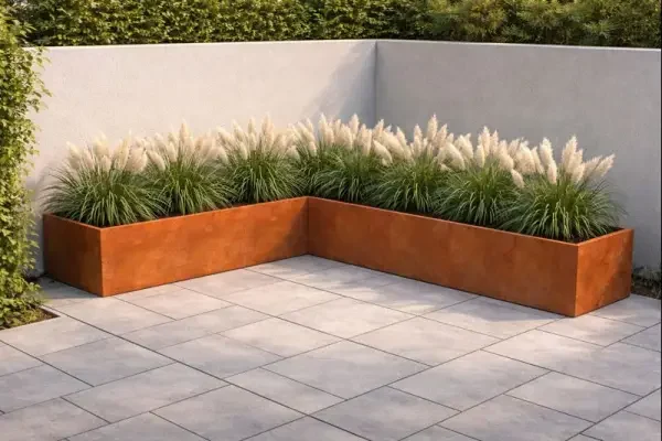L formet højbed i cortenstål placeret i hjørnet af en fliseterrasse med dværg pampasgræs plantet i bedet højbedet måler 280 cm på den korte side 400 cm på den lange side og er 40 cm højt og 40 cm bredt